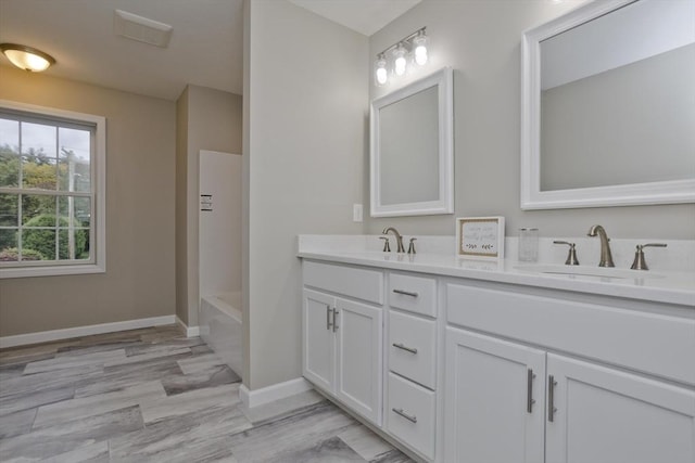 full bath with a bathing tub, a sink, baseboards, and double vanity