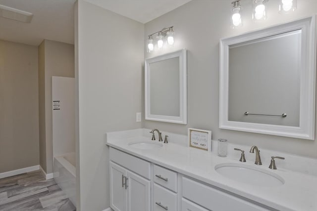 full bath with double vanity, a tub to relax in, a sink, and baseboards