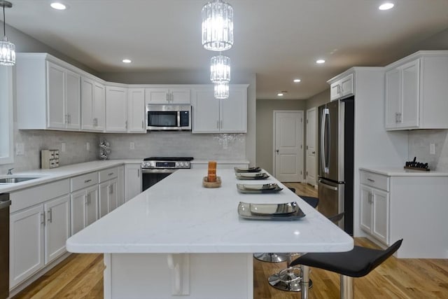 kitchen featuring appliances with stainless steel finishes, light wood-type flooring, white cabinetry, and a kitchen bar