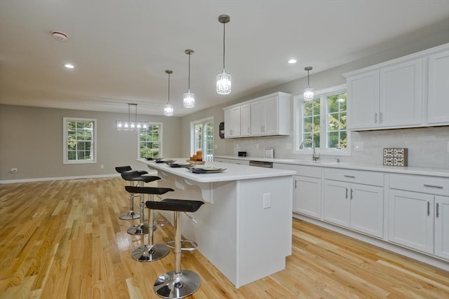 kitchen featuring a kitchen island, white cabinets, light countertops, and a sink