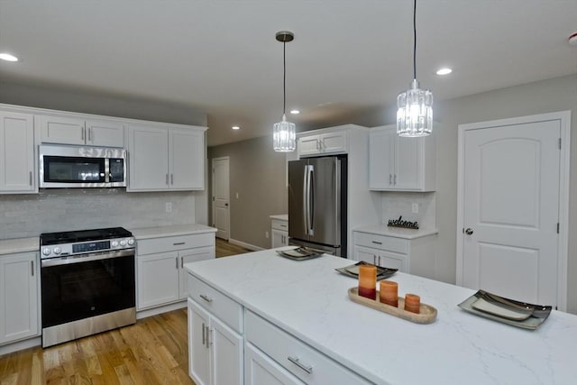 kitchen featuring recessed lighting, stainless steel appliances, white cabinets, hanging light fixtures, and light wood finished floors