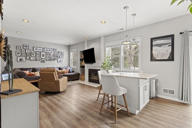 kitchen with a breakfast bar, visible vents, light wood-style flooring, a fireplace with flush hearth, and white cabinetry