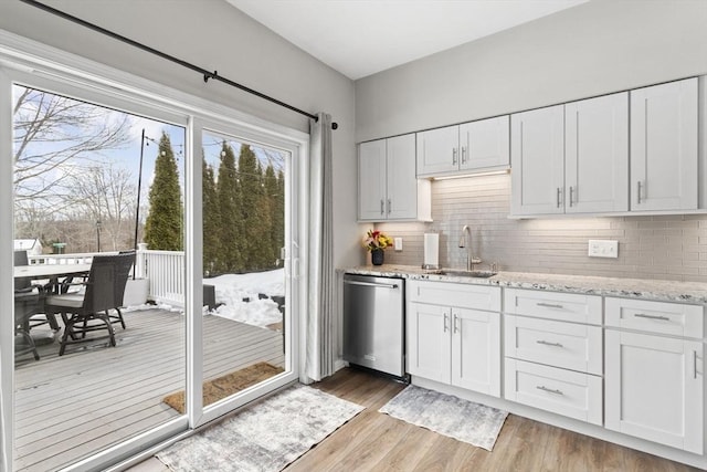 kitchen with stainless steel dishwasher, a sink, light wood-style flooring, and white cabinets