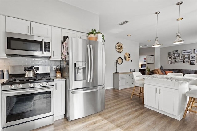 kitchen featuring a breakfast bar, stainless steel appliances, visible vents, backsplash, and open floor plan