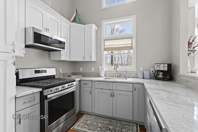 kitchen with gray cabinetry, stainless steel appliances, a sink, white cabinets, and light stone countertops