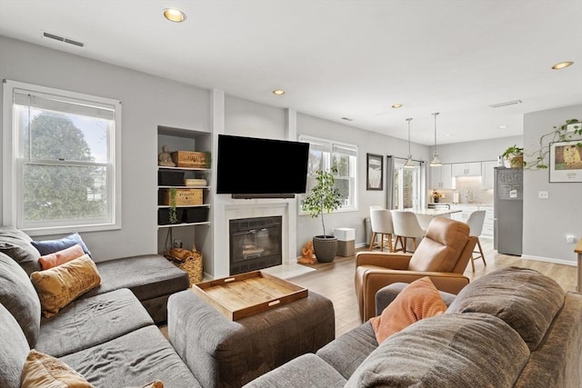 living room with light wood-style flooring, visible vents, and a wealth of natural light