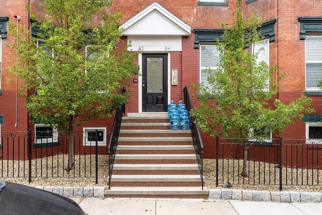 view of exterior entry with brick siding and fence