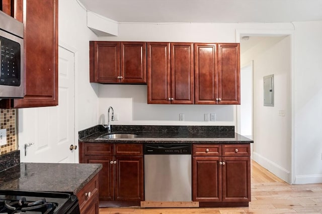 kitchen with backsplash, dark stone countertops, light wood-style floors, stainless steel appliances, and a sink