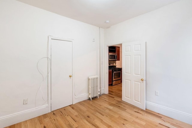 unfurnished bedroom featuring light wood-style flooring, radiator, and baseboards