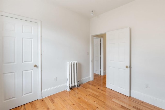 unfurnished room featuring radiator, baseboards, and light wood-style floors