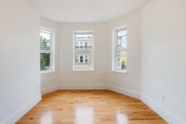 spare room featuring a healthy amount of sunlight, light wood-type flooring, and baseboards