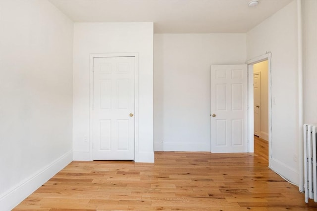 unfurnished bedroom with light wood-type flooring, baseboards, and radiator