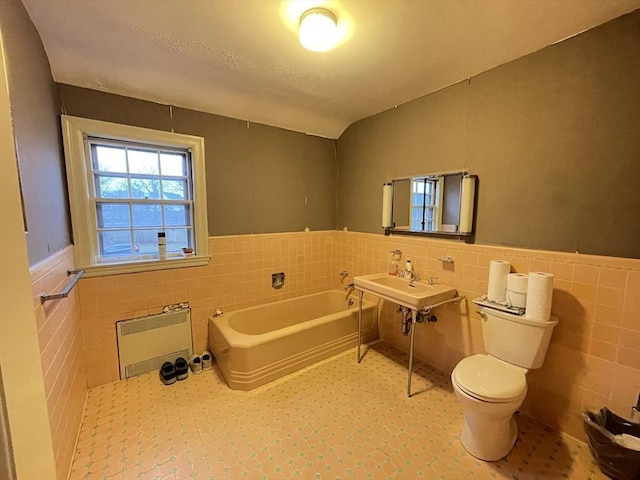 bathroom with toilet, a garden tub, wainscoting, heating unit, and tile walls