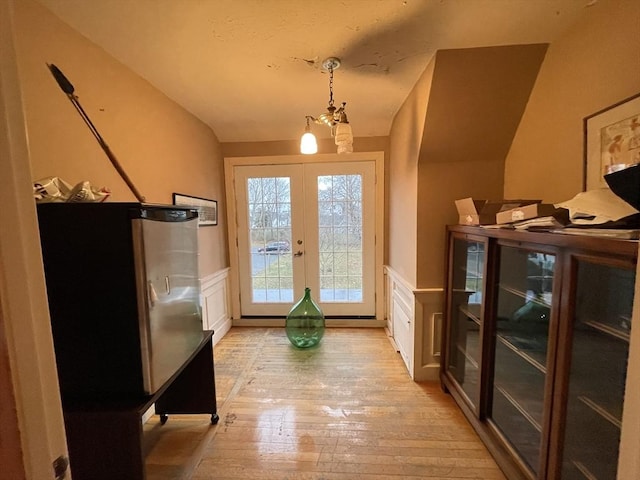 doorway to outside with french doors, light wood-style flooring, wainscoting, and a decorative wall