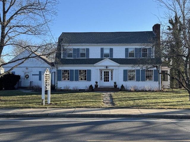 view of front facade with roof with shingles, a chimney, and a front yard