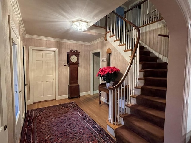 entryway with baseboards, wood finished floors, ornamental molding, and stairs