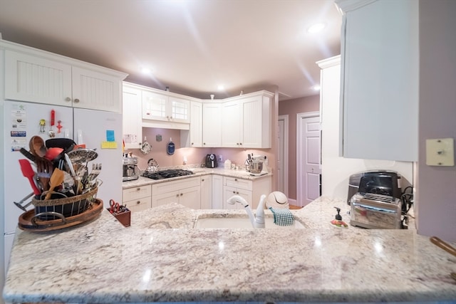 kitchen with light stone counters, sink, white cabinets, and stainless steel gas cooktop