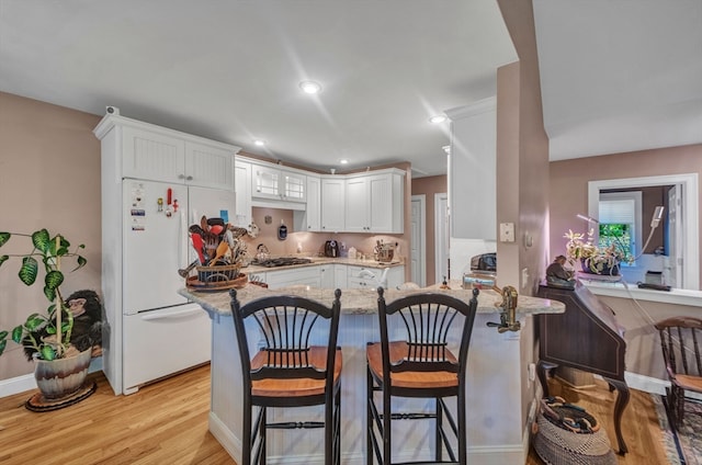 kitchen with white fridge, light hardwood / wood-style floors, kitchen peninsula, and white cabinets