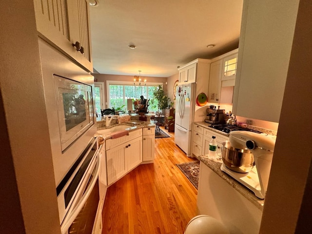 kitchen featuring appliances with stainless steel finishes, decorative light fixtures, light wood-type flooring, and white cabinets