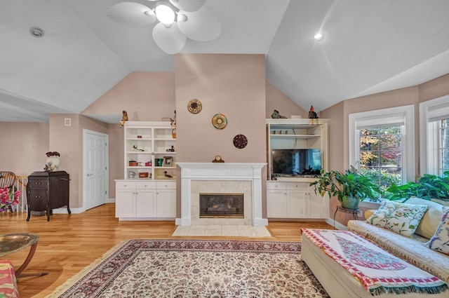 living room with lofted ceiling, a tiled fireplace, light hardwood / wood-style floors, and ceiling fan