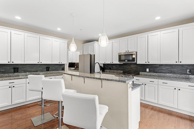 5 Manor Dr Unit B, Hooksett, NH 03106 - kitchen featuring stainless steel microwave, freestanding refrigerator, tasteful backsplash, an island with sink, and white cabinetry