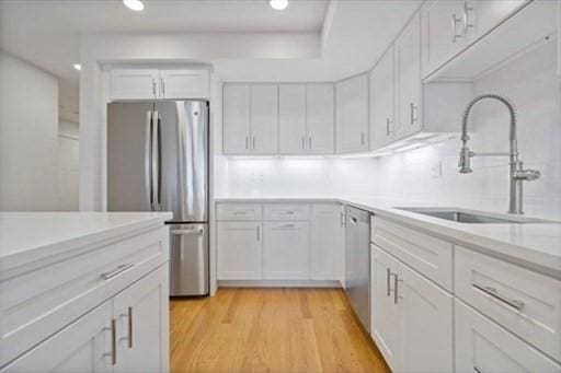 kitchen with stainless steel appliances, light countertops, white cabinetry, and a sink