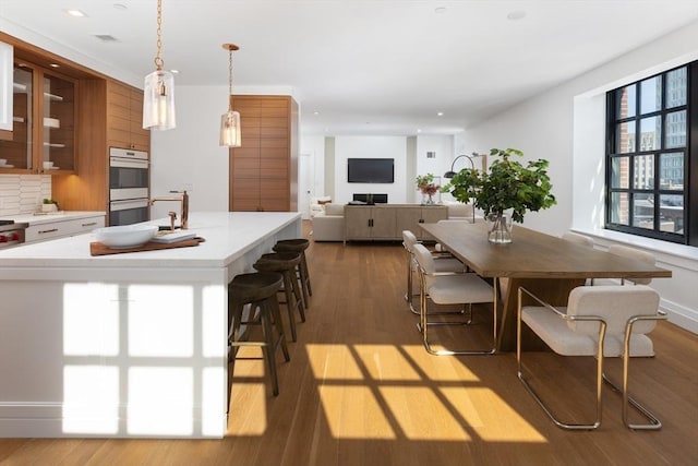 kitchen featuring pendant lighting, light hardwood / wood-style flooring, double oven, tasteful backsplash, and a breakfast bar area