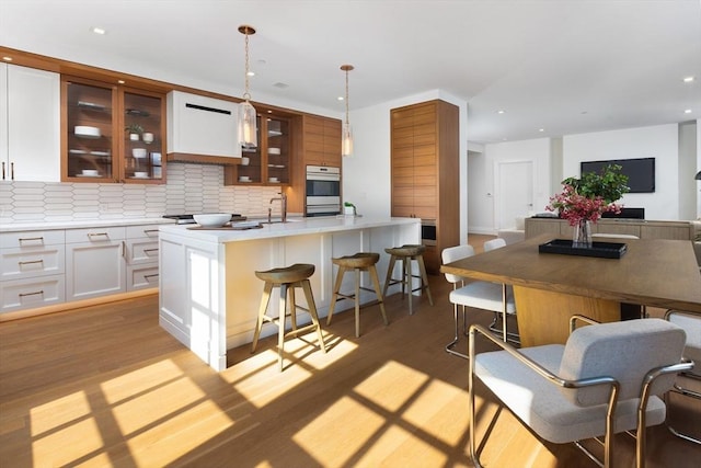 kitchen with light hardwood / wood-style flooring, decorative light fixtures, white cabinets, a kitchen island with sink, and decorative backsplash