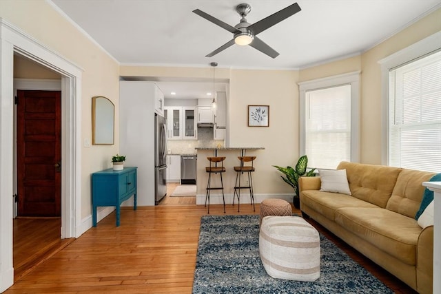 living area featuring ornamental molding, ceiling fan, light wood-style flooring, and baseboards