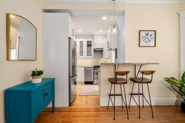 kitchen featuring decorative backsplash, white cabinetry, light wood-style flooring, and a kitchen breakfast bar