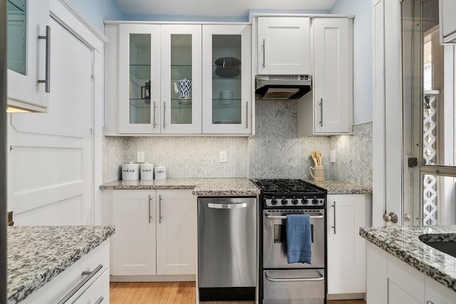 kitchen featuring tasteful backsplash, white cabinets, gas range, glass insert cabinets, and range hood