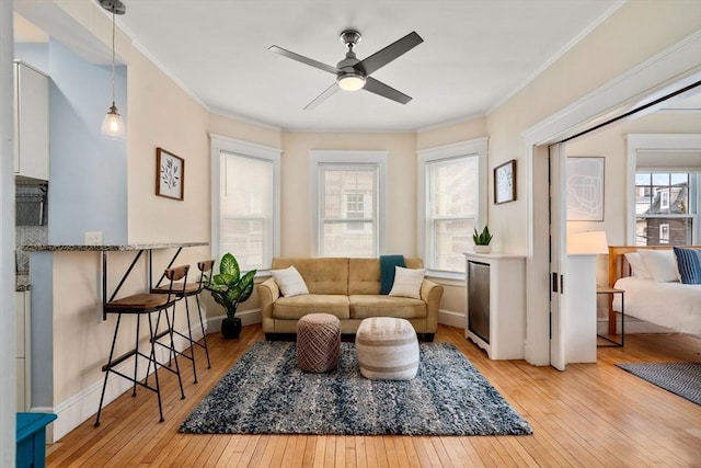 living area with a healthy amount of sunlight, light wood-style floors, ceiling fan, and ornamental molding