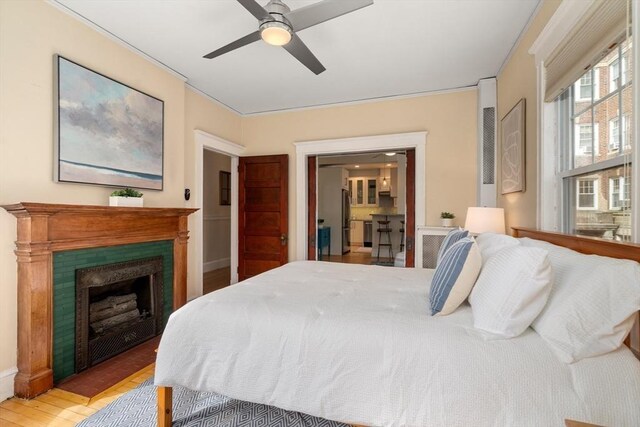 bedroom featuring ceiling fan, freestanding refrigerator, a fireplace, and wood finished floors