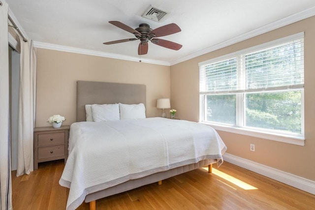 bedroom with a ceiling fan, visible vents, baseboards, light wood finished floors, and ornamental molding