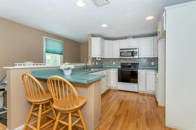 kitchen with electric range, a sink, a peninsula, stainless steel microwave, and visible vents