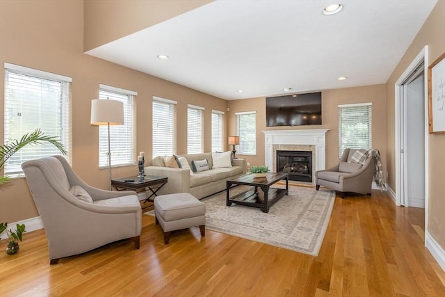 living room featuring a glass covered fireplace, baseboards, and light wood-style flooring