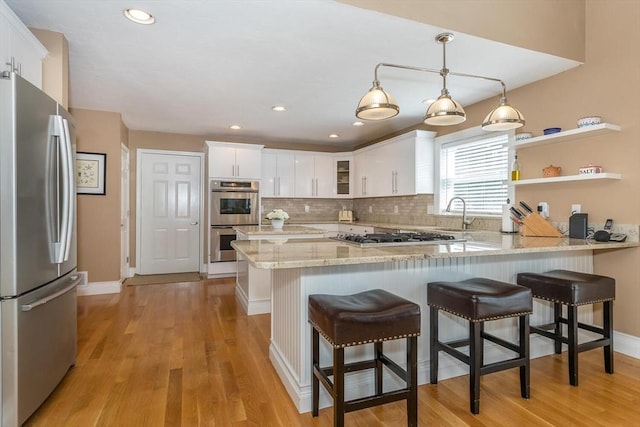 kitchen with a peninsula, light wood-style flooring, appliances with stainless steel finishes, and white cabinetry