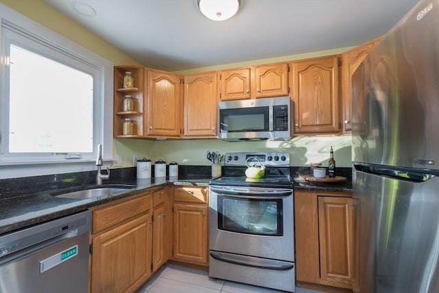 kitchen with a sink, open shelves, stainless steel appliances, dark stone counters, and light tile patterned flooring