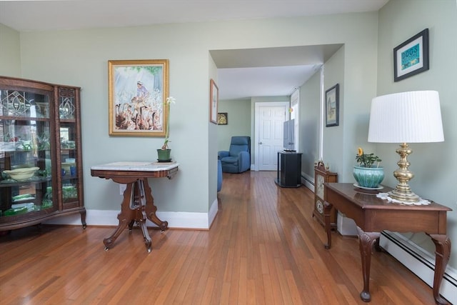 hallway featuring a baseboard heating unit, baseboards, and wood-type flooring