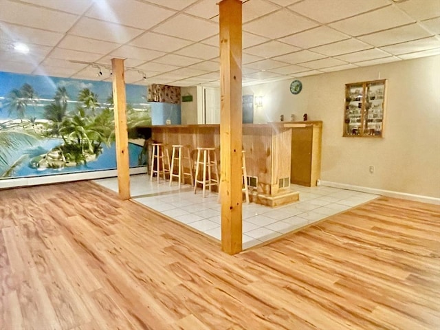 finished below grade area with a paneled ceiling, a baseboard radiator, a dry bar, and wood finished floors