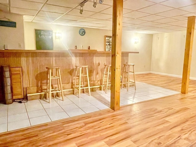 bar featuring baseboards, a drop ceiling, a dry bar, and wood finished floors