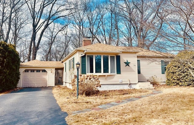 view of front facade featuring a garage, driveway, a chimney, and an outdoor structure