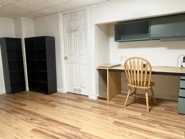 office space featuring light wood-style flooring, visible vents, a drop ceiling, and built in desk