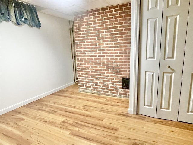 empty room with brick wall, light wood finished floors, and baseboards