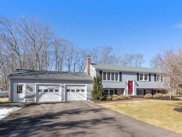 split foyer home featuring aphalt driveway, entry steps, a front yard, a chimney, and a garage