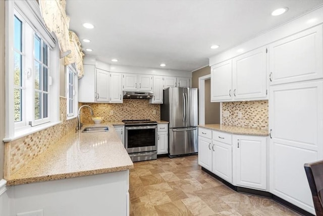 kitchen with light stone counters, a sink, under cabinet range hood, appliances with stainless steel finishes, and white cabinetry