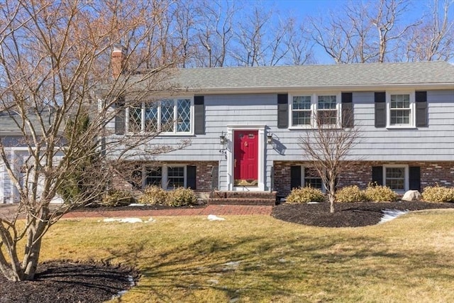 bi-level home with brick siding, a chimney, and a front yard