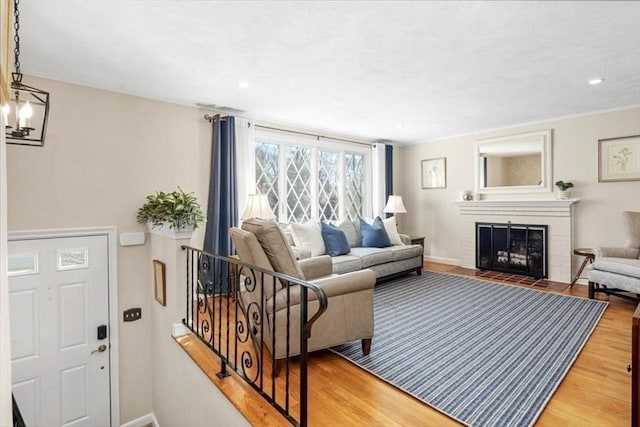 living room featuring wood finished floors, baseboards, recessed lighting, a brick fireplace, and a chandelier