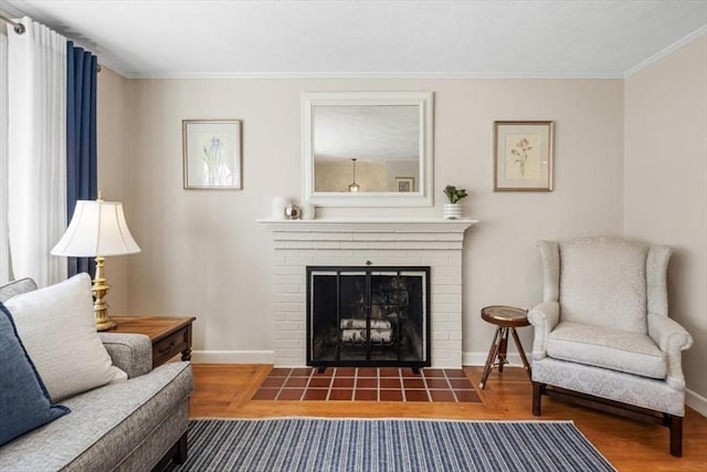 living area featuring baseboards, wood finished floors, a fireplace, and ornamental molding