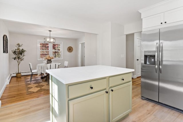 kitchen featuring a kitchen island, stainless steel refrigerator with ice dispenser, light countertops, light wood finished floors, and hanging light fixtures